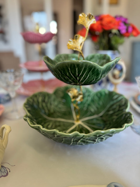 Two-tier stand made from green Bordallo Pinheiro cabbage bowls with gold hardware, styled on a table with glassware and florals.