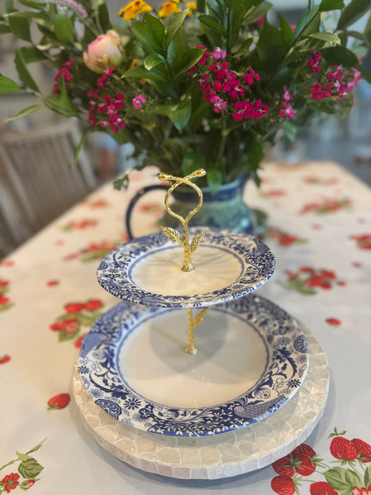 Two-tier stand made from Spode Brocato blue and white china plates with gold handle, styled on a strawberry tablecloth next to a bouquet of fresh garden flowers.