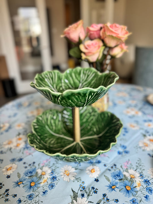 Two-tier Bordallo Pinheiro cabbageware fruit stand with handcrafted wooden support, placed on a floral tablecloth