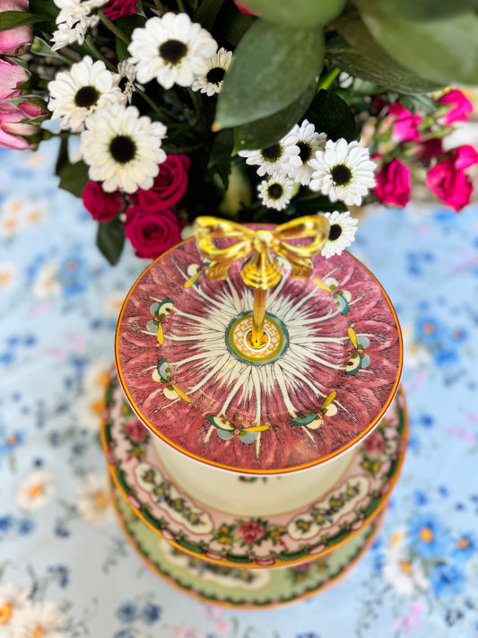 Three-tiered stand with pink bok choy top plate and Williams Sonoma Famille Rose plates, styled with flowers on a floral tablecloth.