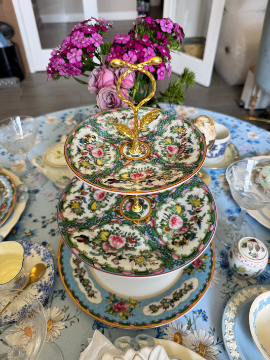 Tiered stand made from Williams Sonoma Famille Rose plates with a gold butterfly handle, surrounded by floral tableware on a blue daisy tablecloth