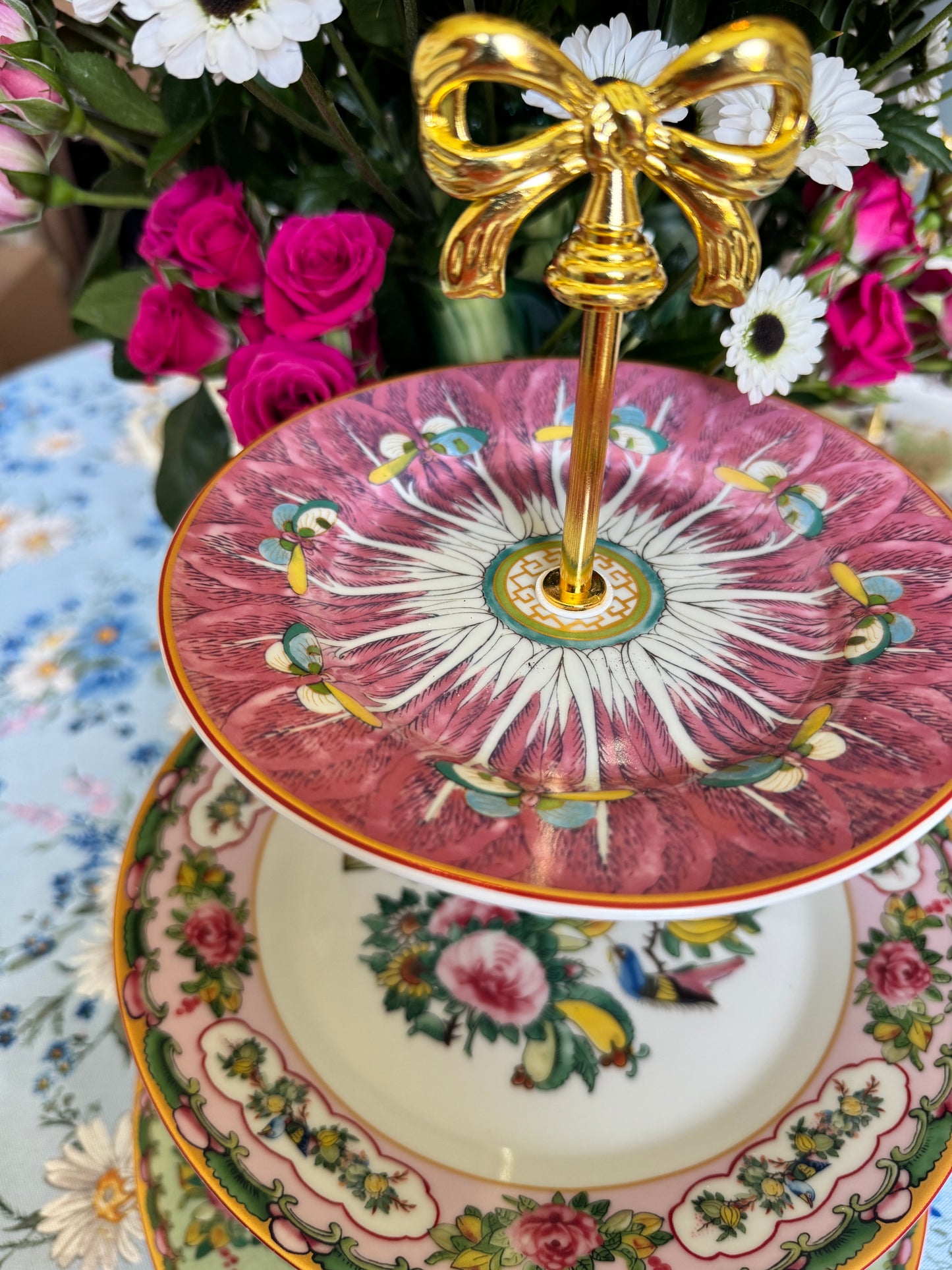 Three-tiered stand with pink bok choy top plate and Williams Sonoma Famille Rose plates, styled with flowers on a floral tablecloth.
