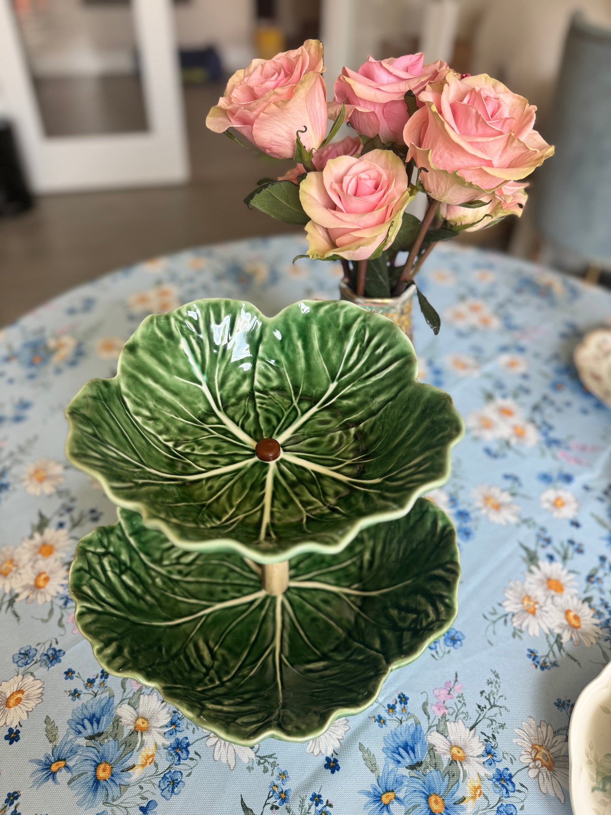 Two-tier Bordallo Pinheiro cabbageware fruit stand with handcrafted wooden support, placed on a floral tablecloth