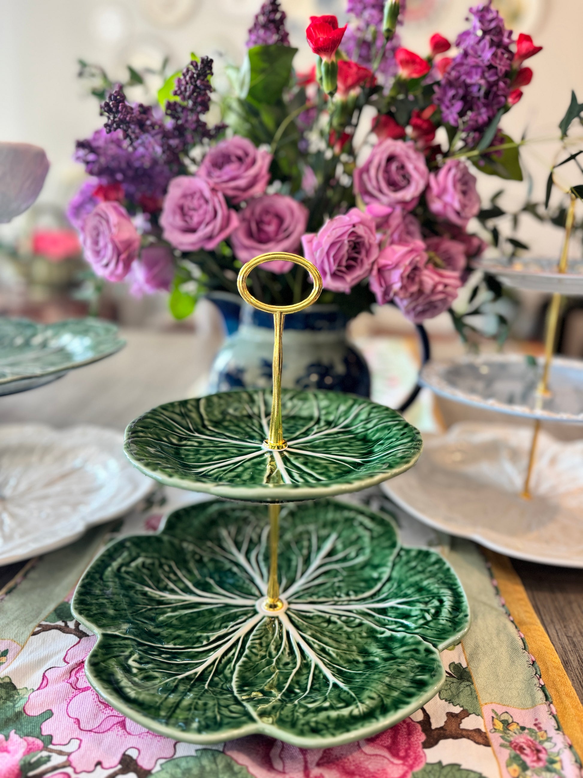 Tiered  stand made from deep green Bordallo Pinheiro cabbage plates with intricate leaf veining, set against a vibrant floral background.