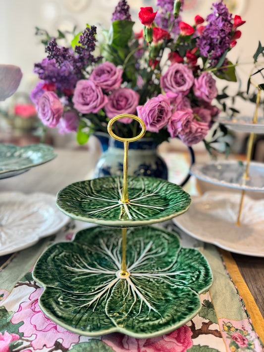 Tiered  stand made from deep green Bordallo Pinheiro cabbage plates with intricate leaf veining, set against a vibrant floral background.