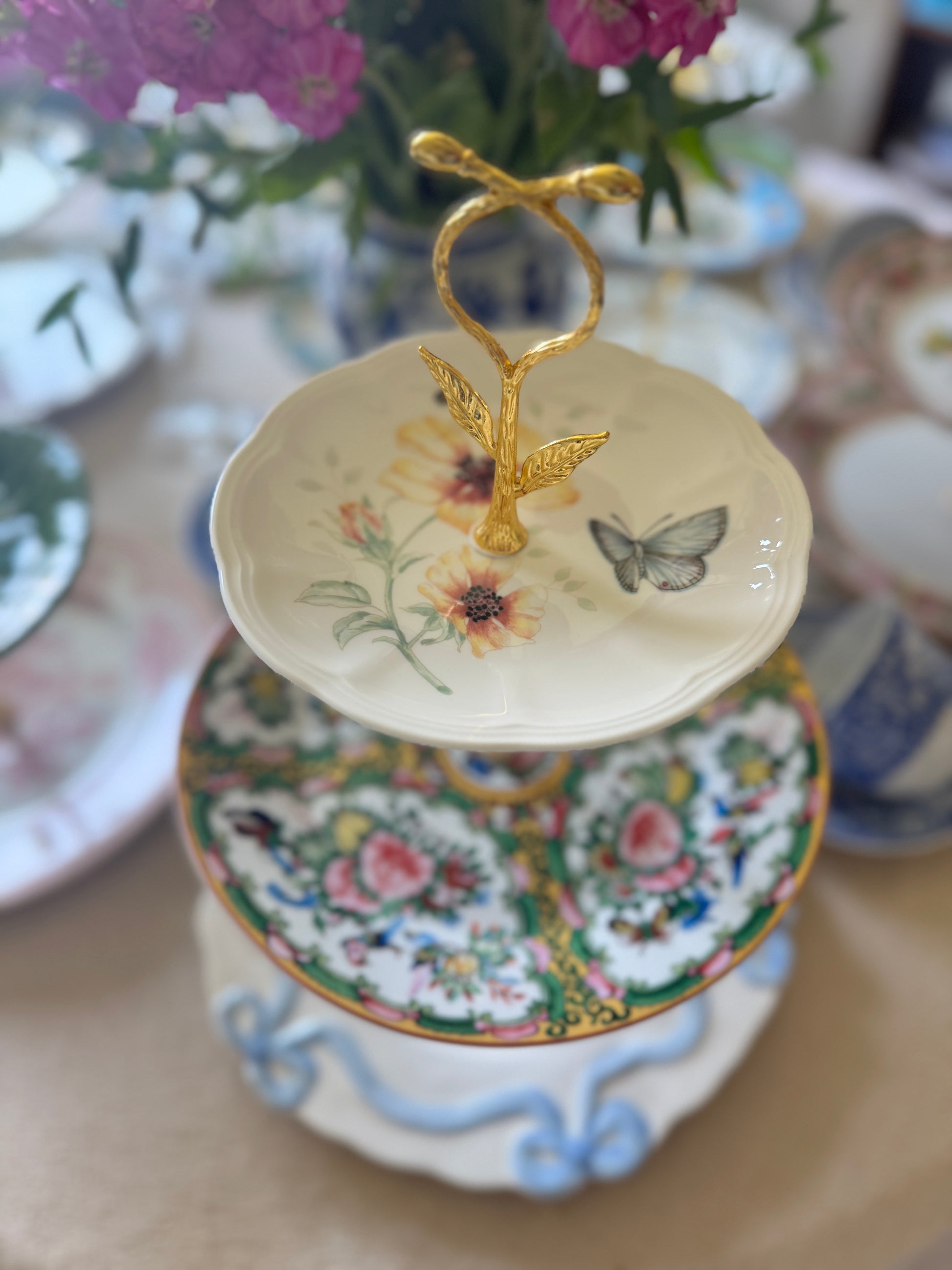 Three-tier serving stand with Lenox Butterfly Meadow plate on top, Famille Rose china in the middle, and Anthropologie bow plate on the bottom, gold hardware, all new plates.