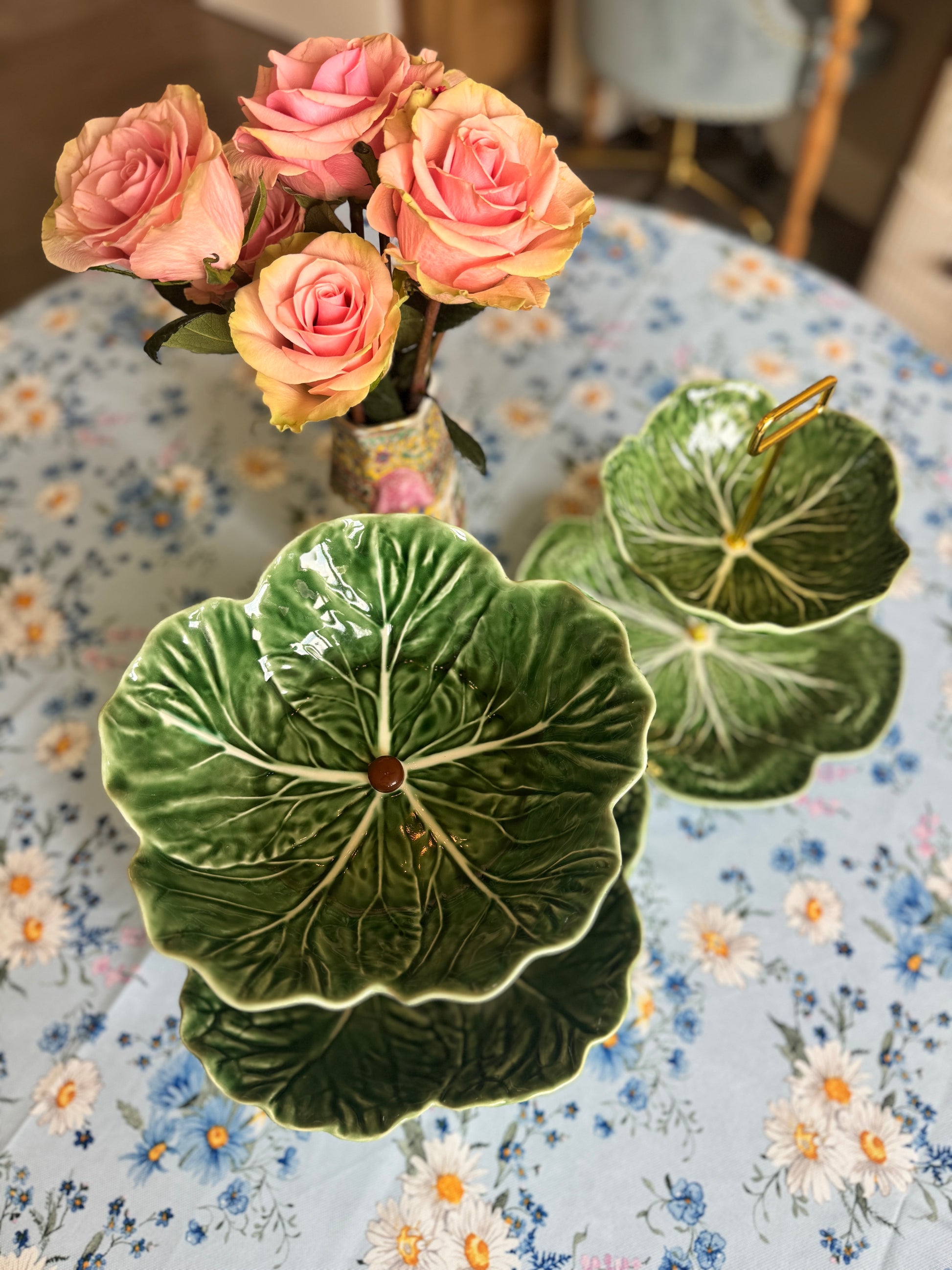 Two-tier Bordallo Pinheiro cabbageware fruit stand with handcrafted wooden support, placed on a floral tablecloth