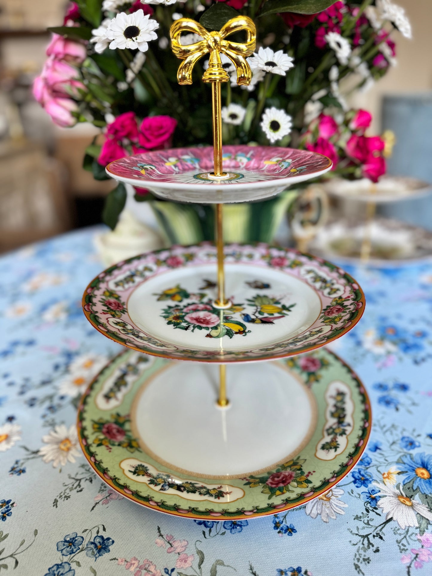 Three-tiered stand with pink bok choy top plate and Williams Sonoma Famille Rose plates, styled with flowers on a floral tablecloth.