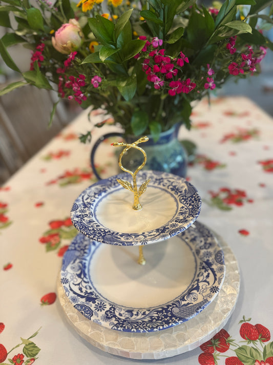 Two-tier stand made from Spode Brocato blue and white china plates with gold handle, styled on a strawberry tablecloth next to a bouquet of fresh garden flowers.
