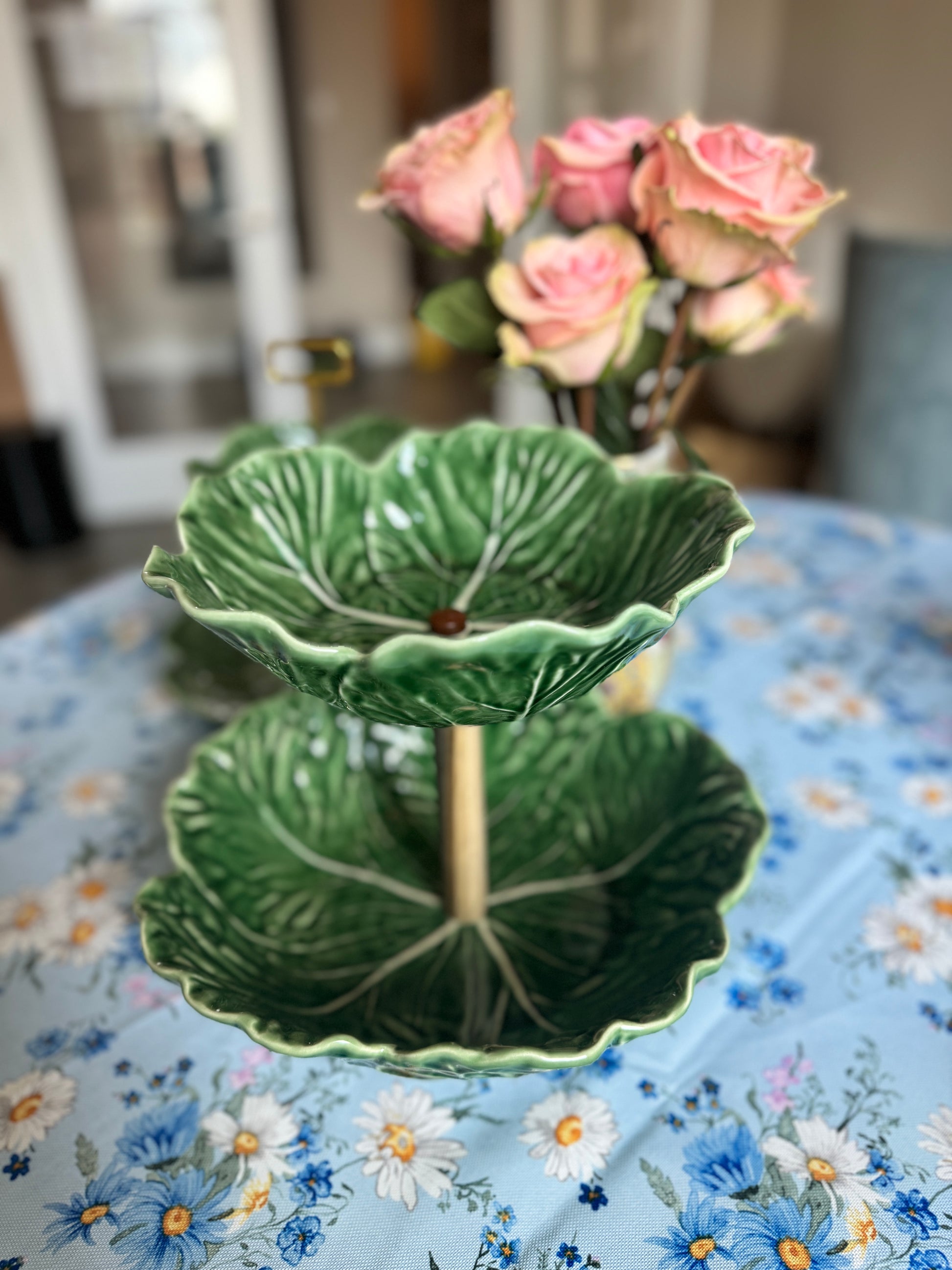 Two-tier Bordallo Pinheiro cabbageware fruit stand with handcrafted wooden support, placed on a floral tablecloth