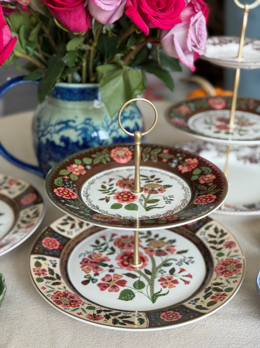 Three-tiered decorative plate with floral design on a table with flowers and another plate in the background.